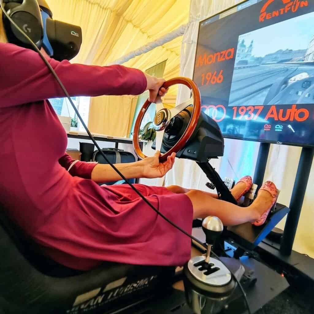 Happy lady in black dress plays virtual reality on vintage motion racing simulator rental on Ceska sporitelna Autoleasing event in Prague.