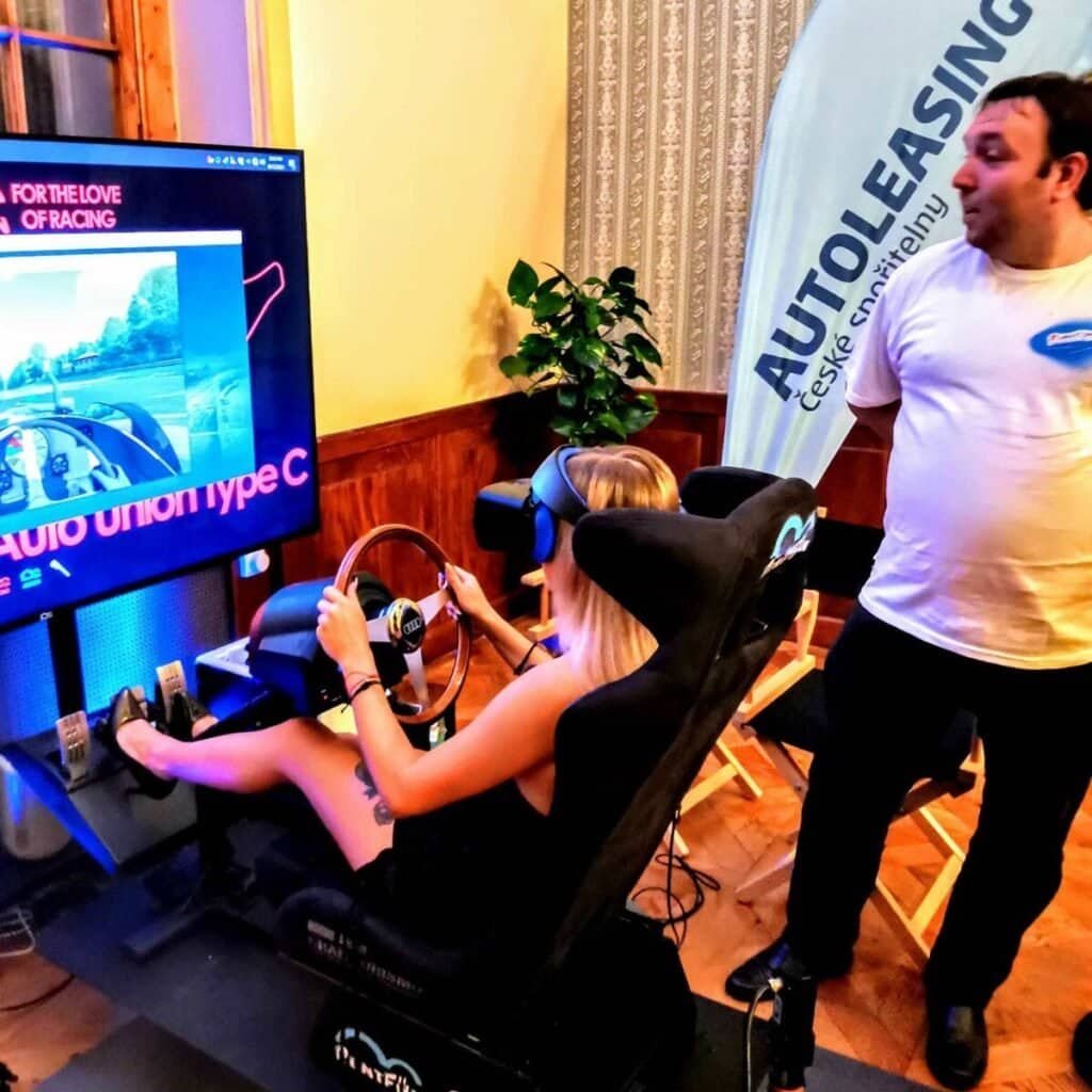 Happy lady in black dress enjoys vintage motion racing simulator rental on Česká spořitelna Autoleasing event.